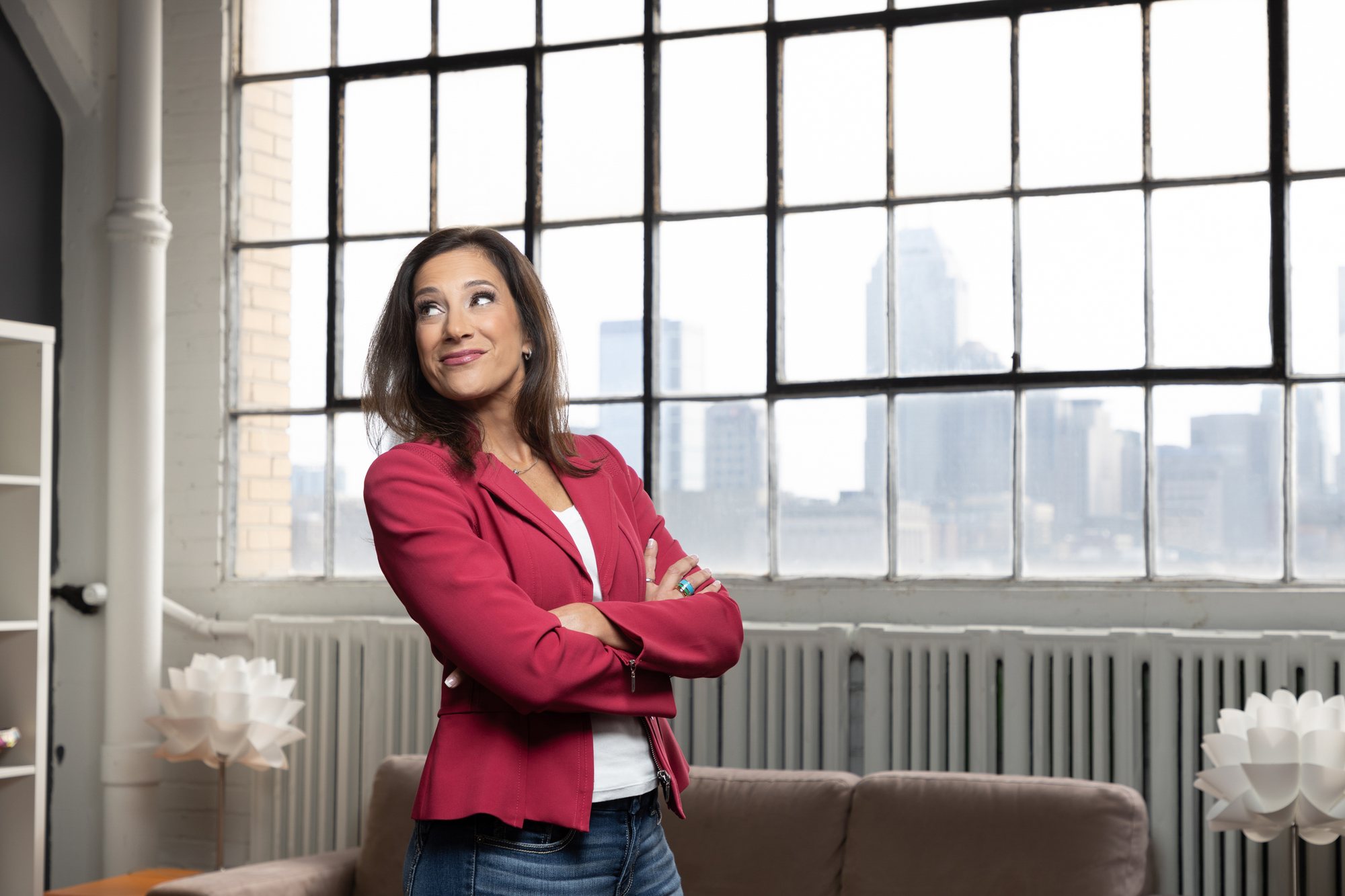 Jennifer Merrell, arms crossed, smiling in a modern loft with large industrial windows